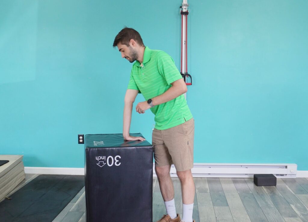 Dr. Jon standing with his palm flat down on a box stretching his right forearm